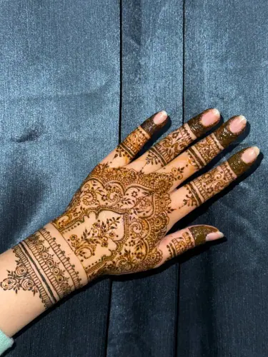 Intricate floral and lattice mehndi extending from the wrist across a hand against blue fabric