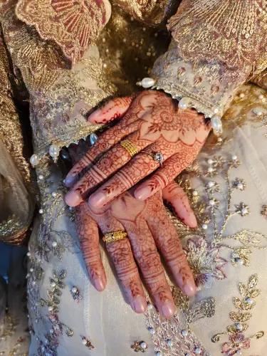 Two hands with floral henna and gold rings against ivory and gold bridal embroidery