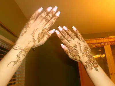 Two henna-decorated hands held up in warm golden light