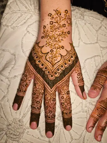 A henna hand with a flowing floral vine and a dark scalloped wrist border