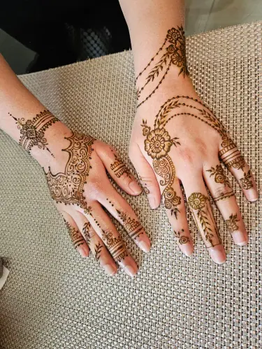 Two hands with matching floral henna vines and leafy fingertips