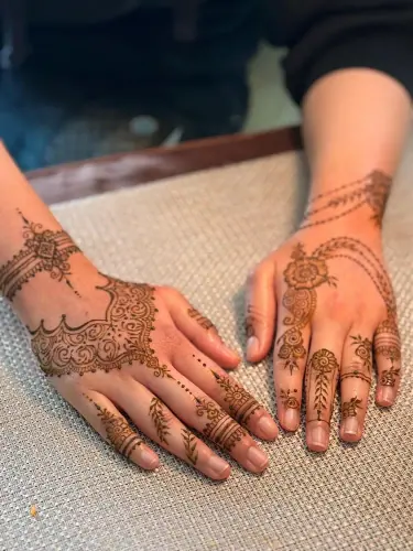 Two hands with flowing floral and paisley henna on pale fabric