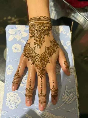 A dense floral henna design with an ornate wrist cuff and lined fingers