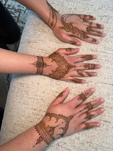 Three hands displaying different floral and leafy henna compositions