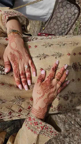 Two hands resting on floral clothing with fine flowing henna patterns