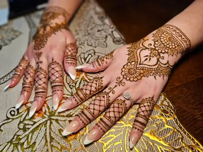 Two hands with floral henna medallions and patterned fingertips on embroidered fabric