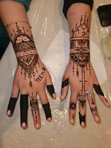 Two hands with matching geometric henna cuffs and crescent moon motifs
