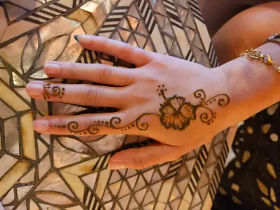A small flower and scrolling henna vine running across a hand
