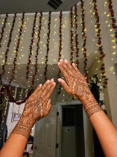 Two intricately decorated henna hands raised in front of hanging fairy lights