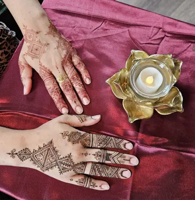 Two hands with floral and geometric henna beside a gold flower-shaped candle holder