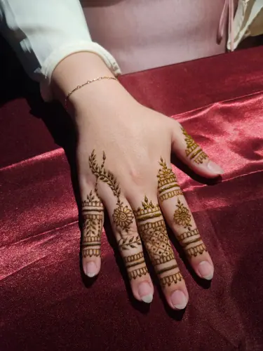 Two hands with small floral henna details and patterned finger bands