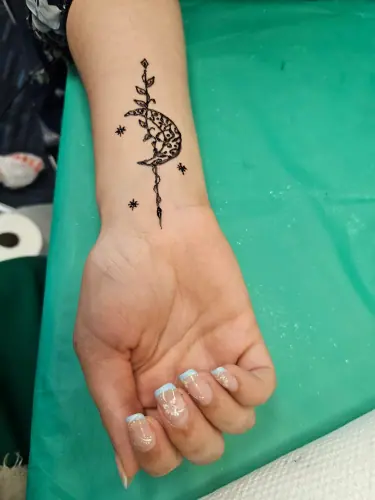 A small crescent and fine floral henna trail on the inner forearm
