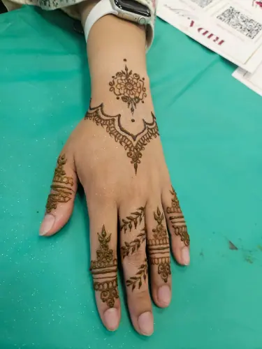 A hand with a floral henna vine and a curved scalloped border on green fabric