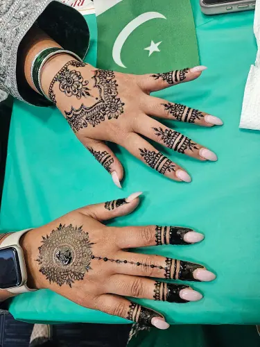 Two hands with contrasting floral henna medallions on green fabric