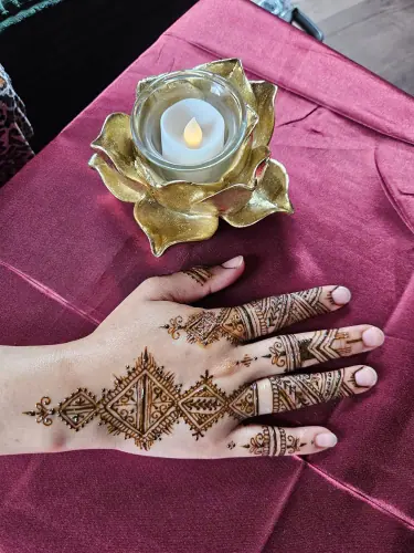 A hand with a geometric floral henna pattern beside a gold candle holder