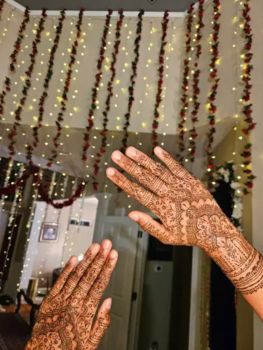 Two hands with detailed floral henna in front of strings of lights