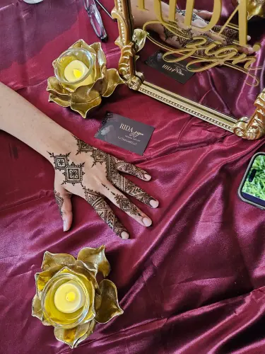 A hand with geometric henna resting on burgundy fabric beside gold decorative flowers