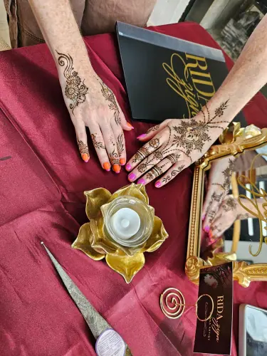 Two hands with floral and geometric henna, bright fingertips and a gold flower-shaped candle holder