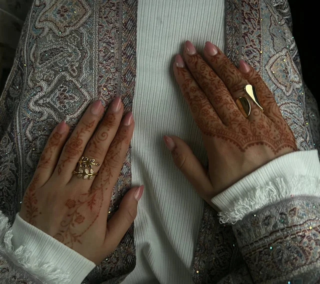 Delicate floral mehndi across two hands resting on pale fabric with mauve embroidery