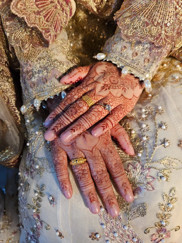 A close view of floral henna patterns and gold rings against embellished bridal fabric